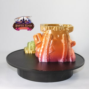 May include: A 3D printed, multi-colored, fantasy-themed miniature castle on a black rotating display stand. The castle is a vibrant mix of orange, yellow, and pink.