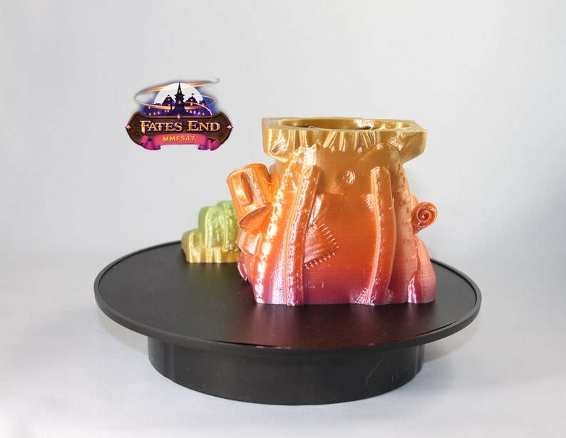 May include: A 3D printed, multi-colored, fantasy-themed miniature castle on a black rotating display stand. The castle is a vibrant mix of orange, yellow, and pink.