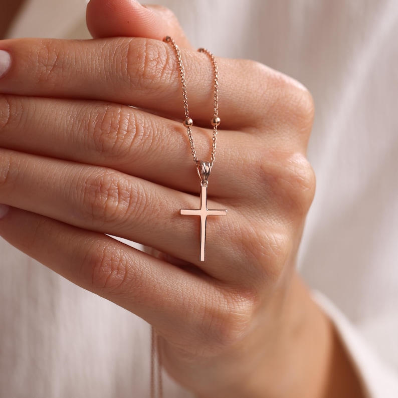 Op de afbeelding: Een ketting van ros&eacute;goud met een delicate kruis hanger en een kralenketting.