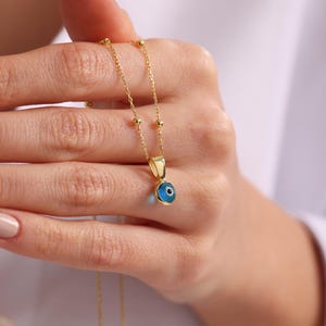 May include: A gold chain necklace with a small blue evil eye pendant. The pendant is round and has a white pupil.