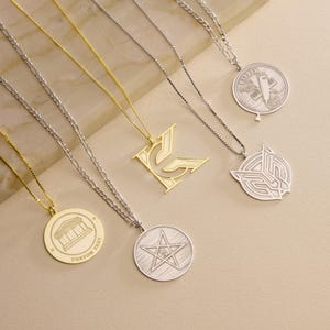 May include: A collection of five metal necklaces featuring various pendants on thin chains. The pendants include a gold letter K, a silver star, a silver barber shop emblem, a silver geometric design, and a gold circular pendant with a building.