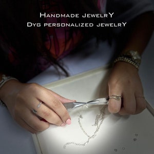 Op de afbeelding: Een persoon werkt aan een zilveren kettingketting met een tang. De tekst "HANDMADE JEWELRY" en "DYG PERSONALIZED JEWELRY" is zichtbaar in de afbeelding.