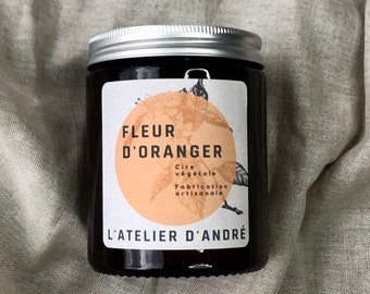 May include: A brown glass jar with a silver lid and a white label. The label has a peach-coloured circle with a black and white illustration of a flower and the text "FLEUR D'ORANGER". The label also includes the text "Cire végétale Fabrication artisanale" and "L'ATELIER D'ANDRÉ".