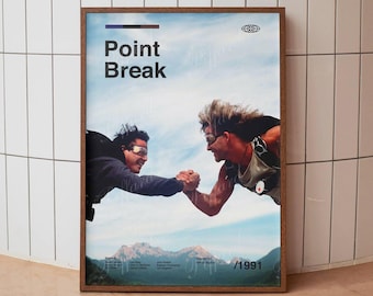 May include: A framed movie poster for Point Break featuring two skydivers in mid-air holding hands against a blue sky and mountain backdrop. The poster includes the title Point Break, a small globe icon, and the year 1991 printed in black text.