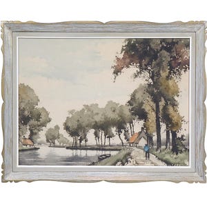 May include: Watercolour painting of a tranquil landscape featuring a river, trees, and cottages. The artwork is presented in a light grey, ornate wooden frame. The painting shows a person walking along a path near the river.