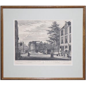 May include: A framed monochrome print of a street scene, featuring buildings, trees, and people. The print is mounted within a white mat and a brown wooden frame. The title is written in Dutch and French.