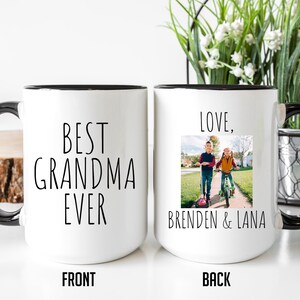 May include: White ceramic mug with a black rim and handle. The front of the mug says "BEST GRANDMA EVER". The back of the mug says "LOVE, BRENDEN & LANA" and has a photo of two children on scooters.