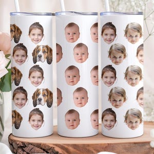 May include: Three white stainless steel tumblers with different patterns of faces printed on them. The tumblers are on a wooden surface with a bouquet of pink roses in the background.