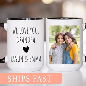 Peut inclure: Mug en céramique blanche avec une anse et un bord noirs. La tasse a une photo de deux enfants souriants et se tenant dans les bras l'un de l'autre sur le côté droit. Le côté gauche de la tasse a le texte "WE LOVE YOU, GRANDPA" avec un cœur noir et le texte "JASON & EMMA".