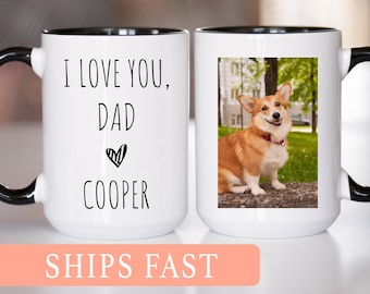 May include: White ceramic mug with a black handle and rim. One side features the text "I LOVE YOU, DAD COOPER" with a heart symbol. The other side displays a photo of a corgi dog. A great gift idea.