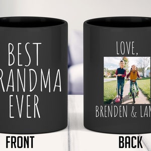 May include: Black ceramic coffee mug with a white inscription on the front that reads "Best Grandma Ever". The back of the mug has a photo of two children, a boy and a girl, walking down a pavement. The text "Love, Brenden & Lana" is below the photo.