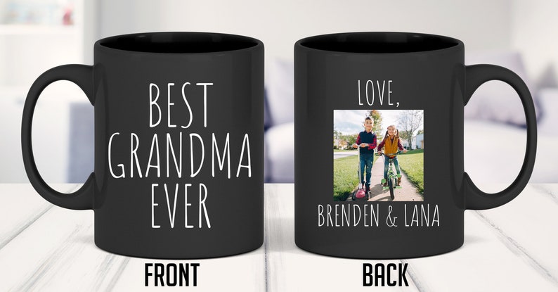 May include: Black ceramic coffee mug with a white inscription on the front that reads "Best Grandma Ever". The back of the mug has a photo of two children, a boy and a girl, walking down a pavement. The text "Love, Brenden & Lana" is below the photo.