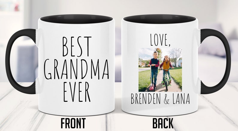 May include: White ceramic coffee mug with a black handle and black rim. The front of the mug says "Best Grandma Ever". The back of the mug has a photo of two children on bikes and says "Love, Brenden & Lana".