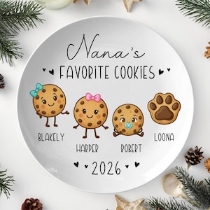 Peut inclure: Une assiette en c&eacute;ramique blanche avec le texte "Nana's Favorite Cookies" et les noms Blakely, Harper, Robert et Loona. L'assiette pr&eacute;sente des personnages de biscuits de dessins anim&eacute;s et une empreinte de patte. L'ann&eacute;e 2026 est &eacute;galement affich&eacute;e.