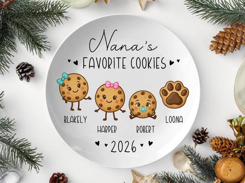Peut inclure: Une assiette en c&eacute;ramique blanche avec le texte "Nana's Favorite Cookies" et les noms Blakely, Harper, Robert et Loona. L'assiette pr&eacute;sente des personnages de biscuits de dessins anim&eacute;s et une empreinte de patte. L'ann&eacute;e 2026 est &eacute;galement affich&eacute;e.
