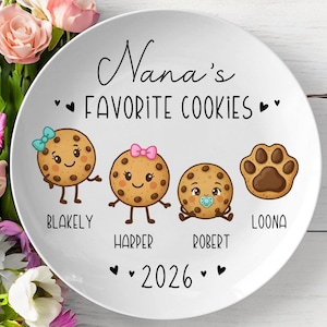 Peut inclure: Assiette en c&eacute;ramique blanche avec l'inscription "Nana's Favorite Cookies" et les noms Blakely, Harper, Robert et Loona. L'assiette pr&eacute;sente des personnages de biscuits de dessins anim&eacute;s et une empreinte de patte. L'ann&eacute;e 2026 est &eacute;galement affich&eacute;e.