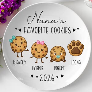 Peut inclure: Assiette en c&eacute;ramique blanche avec le texte "Nana's Favorite Cookies" et l'ann&eacute;e 2026. L'assiette pr&eacute;sente quatre illustrations de biscuits de dessin anim&eacute;, chacune avec un nom : Blakely, Harper, Robert et Loona. Les biscuits ont des visages et des accessoires mignons.