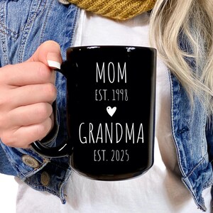 May include: Black ceramic mug with white text that reads "MOM EST. 1998" with a small white heart and "GRANDMA EST. 2025"