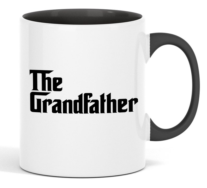 Op de afbeelding: Witte keramische mok met een zwarte binnenkant en handvat. De mok toont de tekst "The Grandfather" in een vetgedrukte, zwarte letter. Het ontwerp is gecentreerd op de buitenkant van de mok en biedt een klassieke en eenvoudige esthetiek.