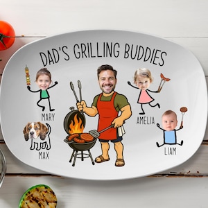 Peut inclure: Assiette ovale blanche avec le texte "DAD'S GRILLING BUDDIES" et des illustrations de dessins anim&eacute;s d'un homme faisant un barbecue avec sa famille et un chien. L'assiette a une fourchette et des tomates sur le c&ocirc;t&eacute;.