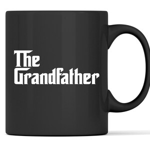 Op de afbeelding: Zwarte keramische mok met witte tekst "The Grandfather". De mok heeft een gebogen handvat en een glanzende afwerking. Geschikt voor warme of koude dranken.