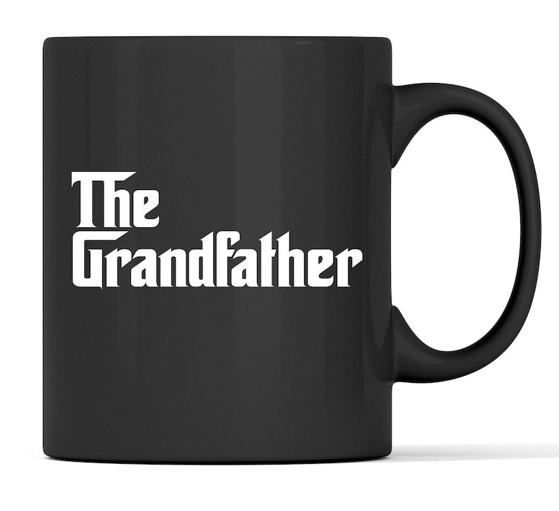 Op de afbeelding: Zwarte keramische mok met witte tekst "The Grandfather". De mok heeft een gebogen handvat en een glanzende afwerking. Geschikt voor warme of koude dranken.
