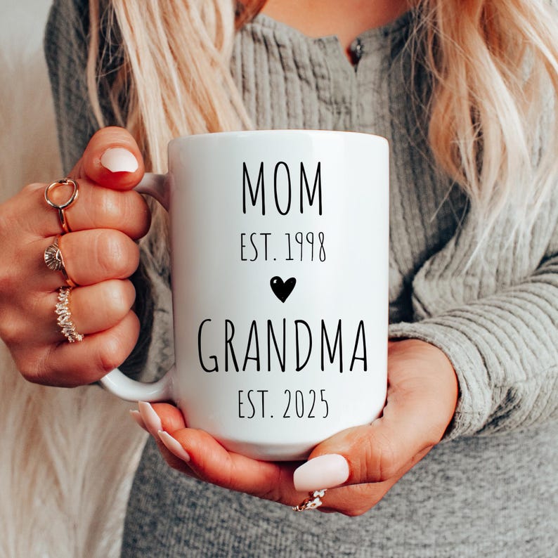 May include: White ceramic mug with black text that reads "MOM EST. 1998" with a black heart and "GRANDMA EST. 2025".