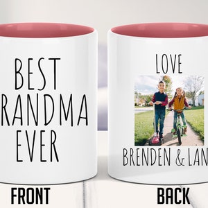 May include: White ceramic mug with a pink rim and handle. The front of the mug says "Best Grandma Ever". The back of the mug has a photo of two children on scooters and says "Love Brenden & Lana".