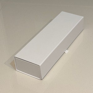 May include: A white cardboard box with a flap on the side. The box is rectangular and has a smooth surface.