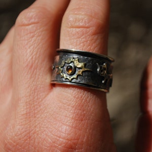 May include: A silver and gold ring with a hammered finish and a small amber gemstone. The ring is decorated with a stylised design of stars and other geometric shapes.