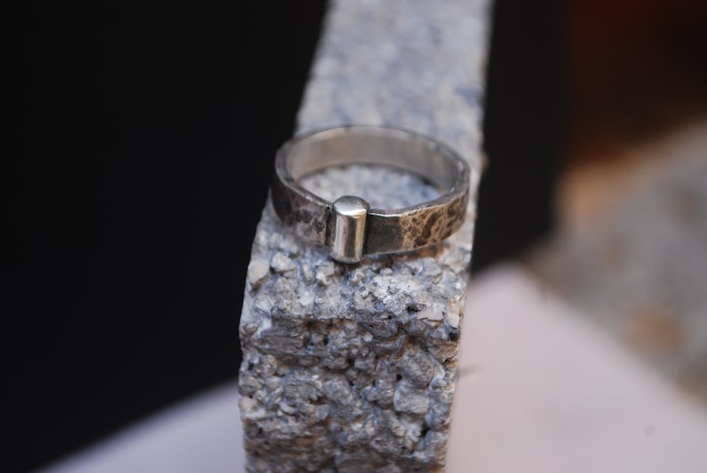 May include: A silver ring with a textured finish and a small, round accent on the top.