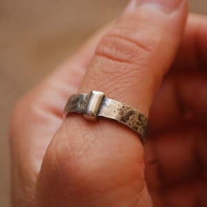 May include: A silver ring with a textured band and a rectangular silver accent piece.