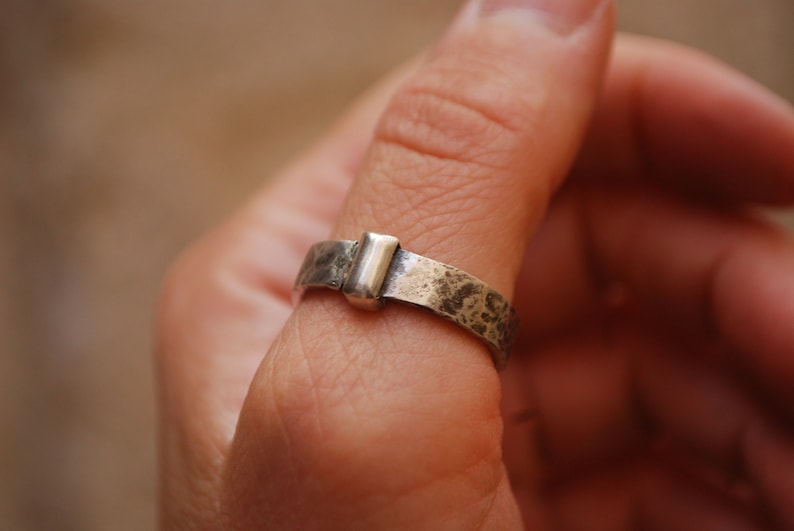 May include: A silver ring with a textured band and a rectangular silver accent piece.