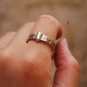 May include: A silver ring with a hammered finish and a rectangular silver accent.