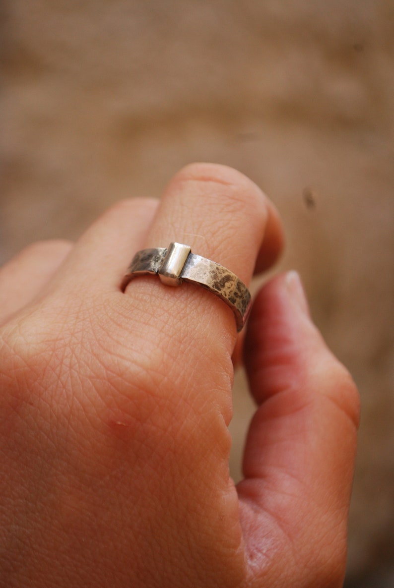 May include: A silver ring with a hammered finish and a rectangular silver accent.
