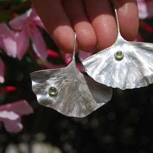 May include: A pair of silver earrings shaped like ginkgo leaves with green gemstone accents.
