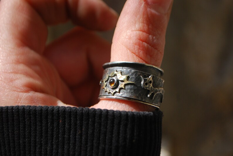 May include: A silver and gold ring with a hammered texture and a small orange gemstone. The ring features a stylised animal design.