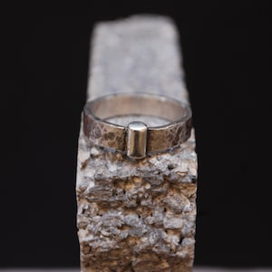 May include: A silver ring with a textured finish and a small, rectangular silver accent on the top.
