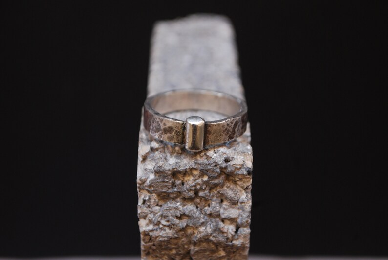 May include: A silver ring with a textured finish and a small, rectangular silver accent on the top.