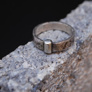 May include: A silver ring with a textured finish and a small, rectangular silver accent.