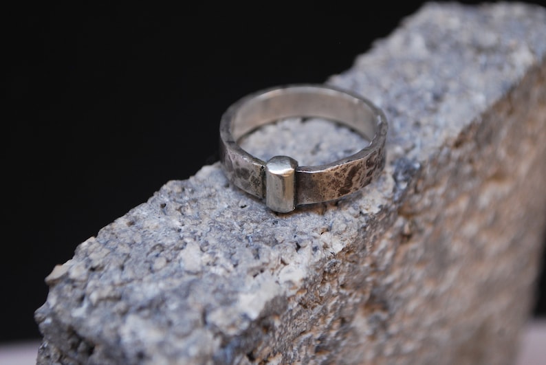 May include: A silver ring with a textured finish and a small, rectangular silver accent.