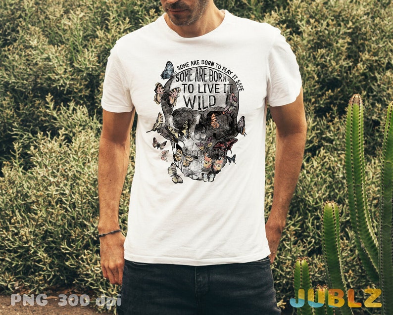 May include: White t-shirt with a skull graphic made of butterflies. The skull has a floral design and the text "SOME ARE BORN TO PLAY IT SAFE SOME ARE BORN TO LIVE IT WILD".