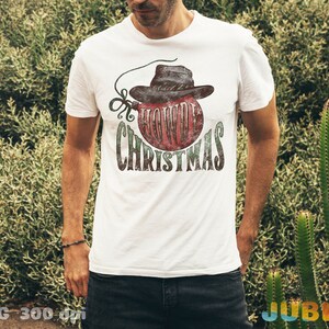 May include: White t-shirt with a red and green Christmas ornament design. The ornament has a cowboy hat on top and the text "Howdy Christmas".