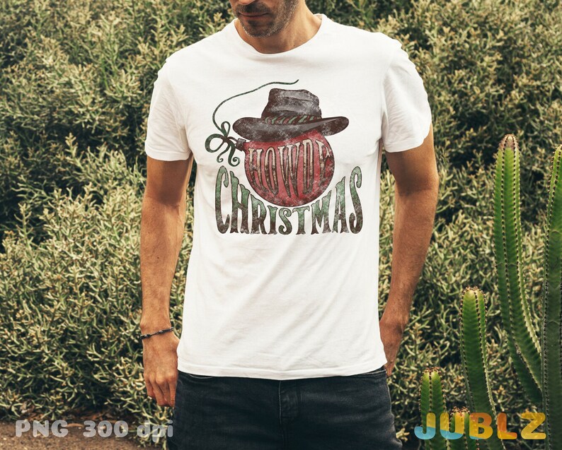 May include: White t-shirt with a red and green Christmas ornament design. The ornament has a cowboy hat on top and the text "Howdy Christmas".