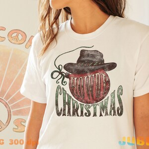 May include: White t-shirt with a vintage-style graphic of a red Christmas ornament wearing a cowboy hat. The text "Howdy Christmas" is printed below the ornament.
