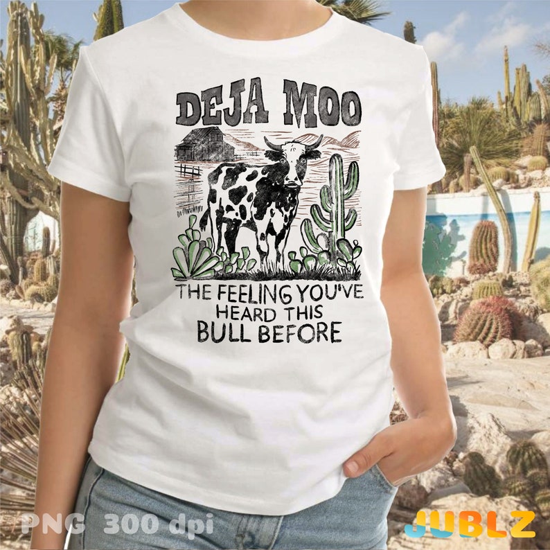 以下が含まれることがあります： 「Deja Moo」と「The feeling you've heard this bull before」のテキストが書かれた、牛とサボテンのヴィンテージスタイルのグラフィックが描かれた白いTシャツ。
