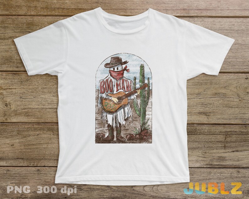 May include: White t-shirt with a graphic of a cartoon ghost wearing a cowboy hat and bandana, playing a guitar, with the text "Boo-Haw" on the shirt. The ghost is standing in front of a cactus.