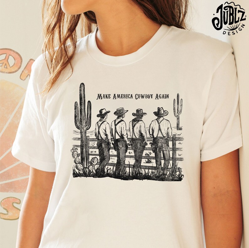 May include: White t-shirt with a black and white illustration of four cowboys standing in front of a fence with cacti. The text "Make America Cowboy Again" is printed on the shirt.