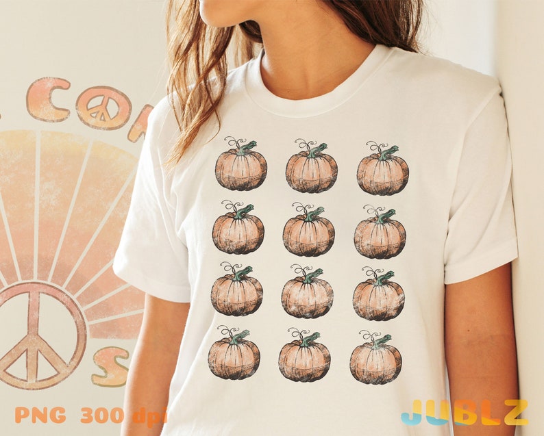 Puede incluir: Camiseta blanca con un patr&oacute;n de 12 calabazas naranjas con tallos verdes. Las calabazas est&aacute;n dispuestas en cuatro filas de tres.