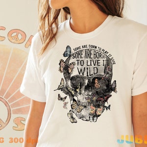 May include: White t-shirt with a skull graphic and butterflies. The skull has the text "Some are born to play it safe. Some are born to live it wild." printed on it.